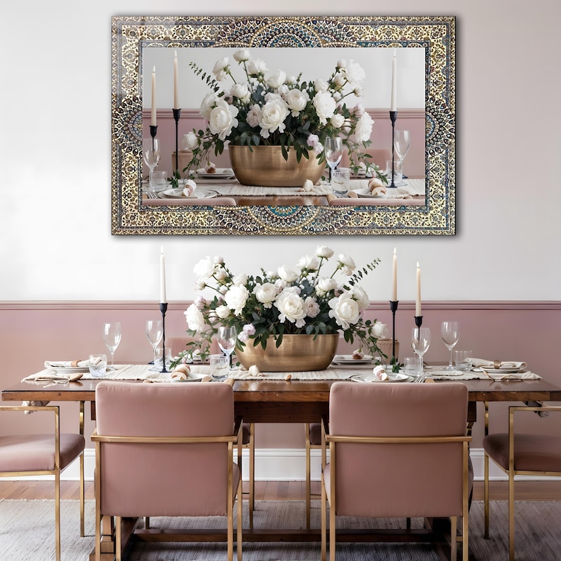 K&ouml;nnte beinhalten: Ein gro&szlig;er rechteckiger Spiegel mit einem verzierten gold- und t&uuml;rkisfarbenen Rahmen h&auml;ngt &uuml;ber einem Esstisch. Der Tisch ist mit einem Blumengesteck in einer goldenen Schale, Kerzen und Gedecken dekoriert. Rosa St&uuml;hle mit goldenen Rahmen vervollst&auml;ndigen die Szene.