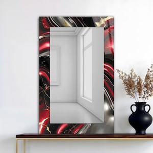 May include: Rectangular wall mirror with a decorative frame. The frame features a swirling pattern of red, black, silver, and gold. The mirror is displayed on a dark brown shelf with a black vase and dried plants.