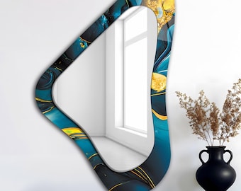 May include: An abstract-shaped wall mirror with a teal, navy, and gold design. The mirror has a unique, curved shape and is displayed on a dark brown surface. A black vase with dried plants is next to the mirror.