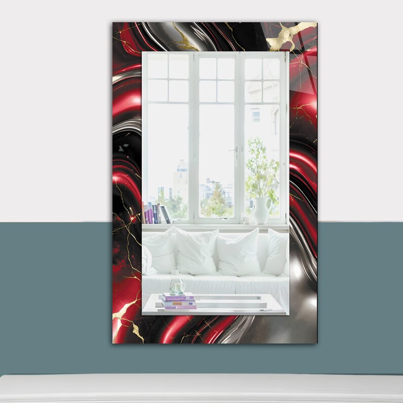 May include: Rectangular wall mirror with a vibrant, abstract design. The frame features a swirling pattern of red, black, and silver with gold accents. The mirror reflects a bright window and a white sofa with pillows.