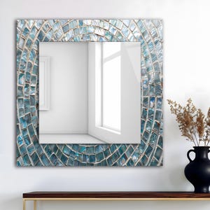 Puede incluir: Espejo de pared cuadrado con un marco de mosaico de azulejos en tonos azules y blancos. El patrón de mosaico se curva alrededor del borde del espejo. El espejo está colgado en una pared blanca.