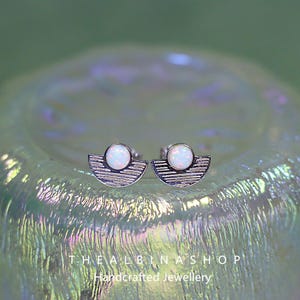 Puede incluir: Un par de pendientes de plata con una piedra de &oacute;palo blanco engastada en forma de media luna. Los pendientes est&aacute;n sobre un fondo blanco.