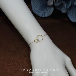 May include: A gold bracelet with two connected circles. The bracelet is on a person's wrist. The text "THEALBINASHOP Handcrafted Jewellery" is at the bottom of the image.