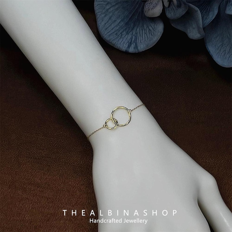 May include: A gold bracelet with two connected circles. The bracelet is on a person's wrist. The text "THEALBINASHOP Handcrafted Jewellery" is at the bottom of the image.