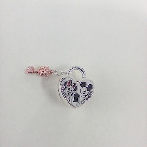 May include: A silver heart-shaped padlock charm with a rose gold key. The padlock features engraved images of Minnie and Mickey Mouse. The key is attached to the padlock with a small chain. The charm is on a white background.