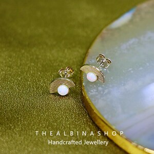 Puede incluir: Un par de pendientes de plata con un dise&ntilde;o de media luna y una piedra de &oacute;palo blanco en el centro. Los pendientes est&aacute;n sobre un fondo blanco.