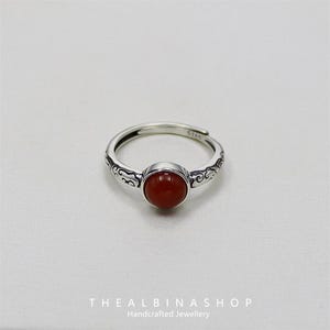 Può includere: Un anello d'argento con un designo ornato e una pietra preziosa rossa. L'anello è contrassegnato con "S925", a indicare che è in argento sterling.