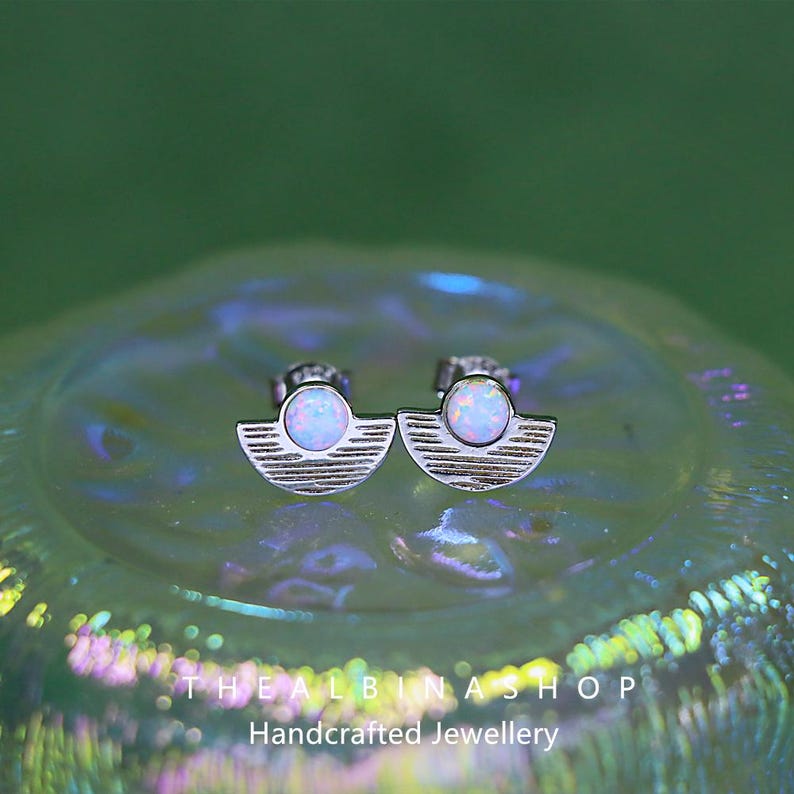 Puede incluir: Un par de pendientes de plata con un dise&ntilde;o de media luna y una peque&ntilde;a piedra de &oacute;palo en el centro. Los pendientes est&aacute;n sobre un fondo blanco.