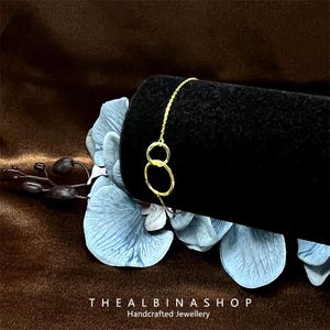 May include: A gold chain bracelet with two interlocking circles. The bracelet is displayed on a black velvet background.