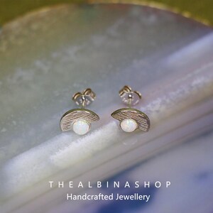 Puede incluir: Un par de pendientes de plata con una piedra de &oacute;palo blanco engastada en forma de media luna. Los pendientes est&aacute;n sobre un fondo blanco.