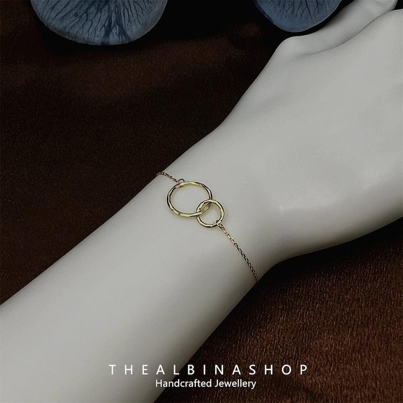 May include: A gold chain bracelet with two interlocking circles. The bracelet is on a person's wrist.