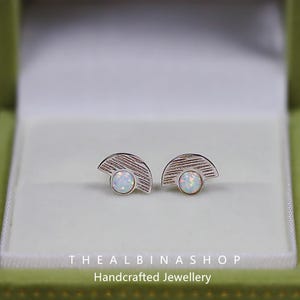Puede incluir: Un par de pendientes de plata con un dise&ntilde;o de medio c&iacute;rculo y una piedra de &oacute;palo blanco en el centro. Los pendientes est&aacute;n en una peque&ntilde;a caja verde con el texto "The Albinashop Handcrafted Jewellery".