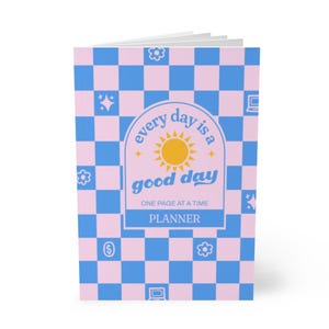 Peut inclure: Un agenda à carreaux rose et bleu avec le texte "every day is a good day" et les mots "ONE PAGE AT A TIME PLANNER" dans un graphique de soleil jaune.