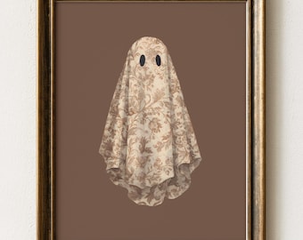 May include: A framed wall art print featuring a ghost figure draped in a beige fabric with a brown floral pattern. The ghost has two simple black oval eyes and is centered against a solid dark brown background within a metallic gold frame.