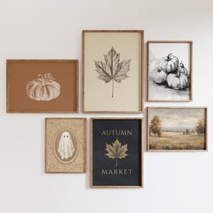 May include: A gallery wall set of six framed prints featuring autumn themes. Includes a white pumpkin on a rust background, a maple leaf on beige, black and white pumpkins, a ghost in an oval frame, a landscape, and an Autumn Market leaf print.