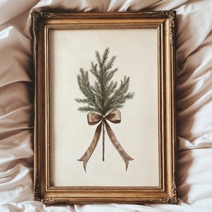May include: A rectangular gold-toned ornate frame containing a print of a green pine branch tied with a brown ribbon. The artwork is centered on a cream-colored background, showcasing a botanical illustration of evergreen needles and a bow.