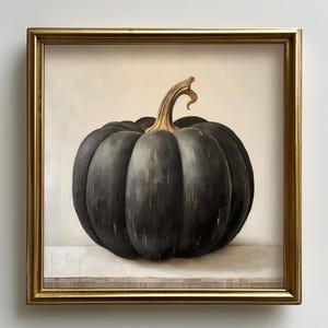 May include: A framed painting of a black pumpkin with a curved stem. The pumpkin is set against a neutral background and rests on a light-colored surface. The frame is gold-colored.