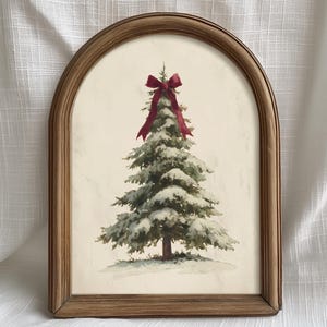 May include: An arched wooden frame containing a print of a snow-covered evergreen tree. The tree is decorated with a single dark red ribbon bow at the top. The background of the print is a light cream colour, and the tree sits on a snowy base.