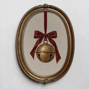 May include: A brass jingle bell hangs from a deep red satin ribbon tied in a bow, centred within an ornate oval gold frame. The bell features a classic spherical shape with a horizontal seam and two curved cutouts at the bottom, set against a neutral background.