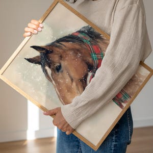 Vintage style horse wearing a red and green tartan bow with snow falling on a beige background, rustic printable farmhouse Christmas wall art.