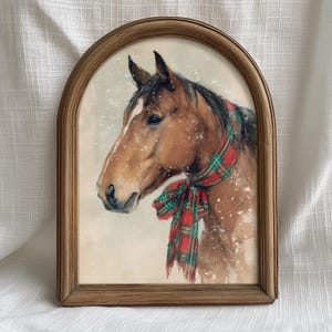Vintage style horse wearing a red and green tartan bow with snow falling on a beige background, rustic printable farmhouse Christmas wall art.