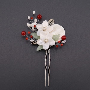 May include: A decorative hair pin featuring white flower accents with pearl centers, red beads, and green leaves. The pin has a silver-colored metal base and a decorative bird. This hair accessory is suitable for special occasions.