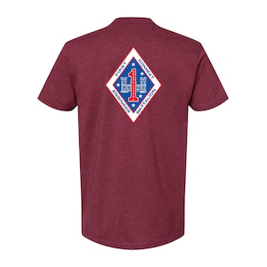 May include: Maroon t-shirt featuring a diamond-shaped emblem with the text "FIRST ENGINEER COMBAT BATTALION" in white, blue, and red. The emblem includes a number 1 and a building design. The shirt is a solid color.