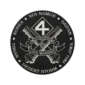 May include: A circular black emblem featuring a white graphic of crossed cannons behind a diamond shape with the number 4. Banners read 3rd BATTALION and 14TH MARINES. The border text includes ROI-NAMUR, SAIPAN, IWO JIWA, DESERT STORM, TINIAN, and KOREA.