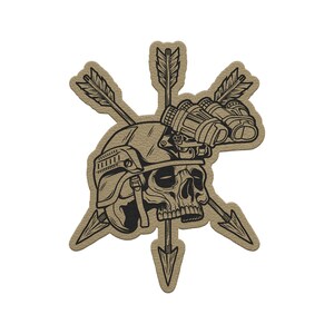 May include: A tan patch featuring a skull wearing a helmet and night vision goggles, pierced by three arrows. The design is outlined in black, creating a striking contrast against the tan background. The patch has a textured appearance.