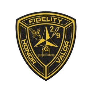 May include: A black and yellow patch with the words "FIDELITY", "HONOR", and "VALOR". The patch features an eagle, a star, the numbers "2/9", and the phrase "HELL IN A HELMET".