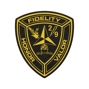 May include: A black and yellow patch with the words "FIDELITY", "HONOR", and "VALOR". The patch features a yellow eagle, a star, the numbers "2/9", and the phrase "HELL IN A HELMET".