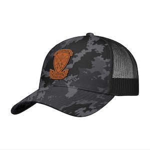 May include: A black and gray camouflage baseball cap with a mesh back. The cap features a brown leather patch with the text "5th Battalion" and "Marines Retreat Hell". The cap has a curved brim.