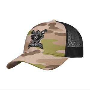 May include: A camouflage baseball cap with a black mesh back. The front of the cap features a patch with the words "2nd Battalion" and "2nd Marines" along with other text and a crest.