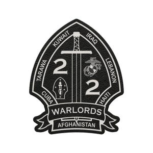 May include: A black and white patch with a sword, the number 2, and the words "WARLORDS" and "AFGHANISTAN". The patch also includes the names of several countries, including Kuwait, Iraq, and Lebanon. The patch has a textured appearance.