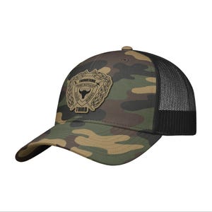 May include: Camouflage baseball cap with a black mesh back. The cap features a patch with the text "Thundering Third Battalion Marines". The cap is a blend of green, brown, and tan colors.