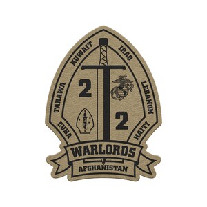 May include: Tan and black patch with a sword, the number 2, and the words "WARLORDS" and "AFGHANISTAN." The patch also includes the names of several countries and a Marine Corps emblem. The patch is shaped like a shield.