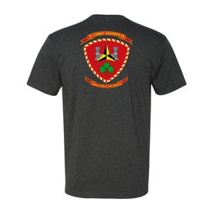 May include: Dark gray t-shirt featuring a crest with the text "3D COMBAT ENGINEER BN" and "DEMOLITION IS THE MISSION." The crest is red with a yellow border, a green shamrock, and a black and yellow design.