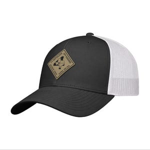 May include: Black and white trucker hat with a curved brim. The front panel is black, and the back is white mesh. A tan patch with text and a graphic is on the front.