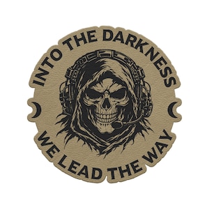 May include: Tan patch with a black skull wearing a headset and a hood. The patch has the text "INTO THE DARKNESS WE LEAD THE WAY" in a circular design. The patch has a textured appearance and a unique shape.