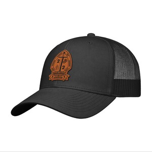 May include: Black trucker hat with a curved brim and mesh back. The hat features a brown leather patch with the text "WARLORDS AFGHANISTAN" and other text and graphics.