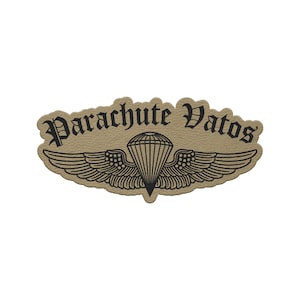 May include: Tan patch with the words "Parachute Vatos" in a gothic font. Below the text is a black illustration of a parachute with wings. The patch has a textured appearance.