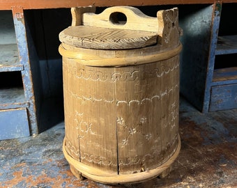 Puede incluir: Un cubo de madera con una tapa tallada y un asa. El cubo está decorado con tallas intrincadas y tiene un acabado de madera natural.