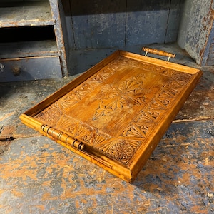May include: A rectangular wooden serving tray with intricate carved details. The tray has two wooden handles and a natural wood finish.