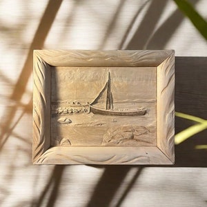 May include: A wooden framed picture with a carved image of a sailboat on the water. The frame has a wavy design.