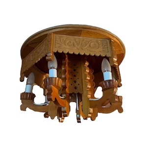 May include: A wooden chandelier with a carved design. The light fixture has a round top and a series of decorative elements. The chandelier has three light bulbs. The wood is a light brown color.