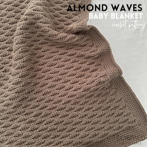 May include: A brown crocheted baby blanket with a textured wave pattern. The blanket is folded in half and the text "ALMOND WAVES BABY BLANKET crochet pattern" is visible in the top right corner.