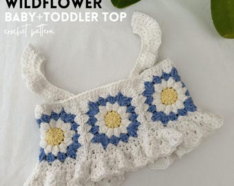 May include: White crochet baby and toddler top with blue and yellow flower accents. The top has a ruffled bottom and straps. The text "LITTLE WILDFLOWER BABY + TODDLER TOP crochet pattern" is at the top of the image.