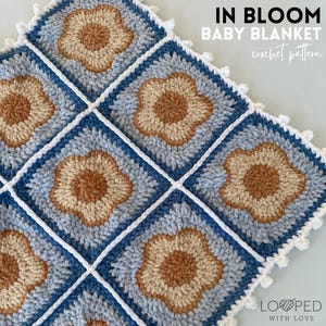 Peut inclure: Une couverture pour bébé en crochet avec une bordure bleue et blanche et un motif répétitif de fleurs brunes et beiges. La couverture est intitulée "In Bloom Baby Blanket crochet pattern".