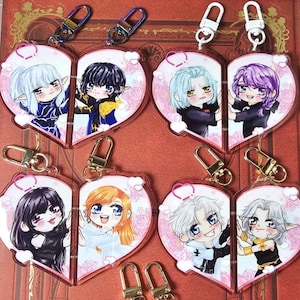Puede incluir: Seis charms de acrílico en forma de corazón con personajes de anime coloridos. Cada charm presenta dos personajes, uno a cada lado del corazón. Los charms están unidos a llaveros de oro y plata.