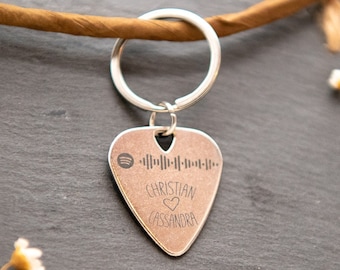 Pode incluir: Um chaveiro de palheta de guitarra prateado com um código de barras preto e branco, as palavras "Christian" e "Cassandra" e um símbolo de coração.